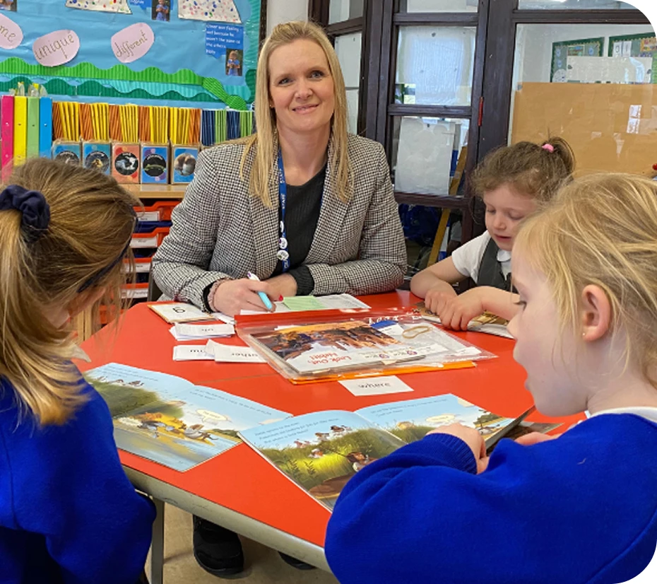 Natasha-level-5-specialist-TA-quote TA Natasha Smith sits at a desk reading with school children